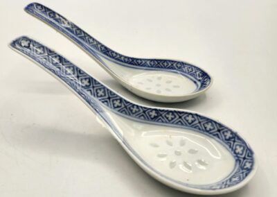 Two ceramic spoons with blue floral patterns and perforated bowls.