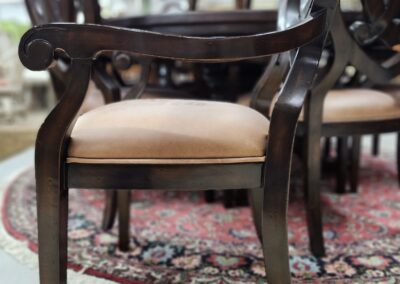 Elegant wooden chair with curved armrests and beige cushion on a patterned rug.