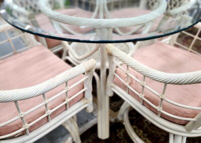 White wicker dining chairs with pink cushions around a glass-top table.
