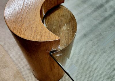 Curved wooden furniture leg supporting a glass top.
