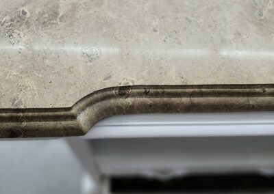 Close-up of a chipped and stained beige marble countertop edge.