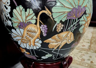 Decorative ceramic vase with painted birds and foliage on a wooden stand.