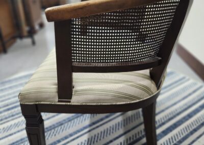 Wooden chair with a cushioned seat and woven backrest on a striped rug.