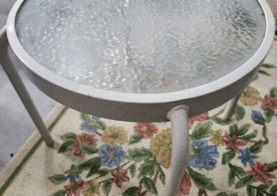 Round glass-top table with white frame on floral carpet.