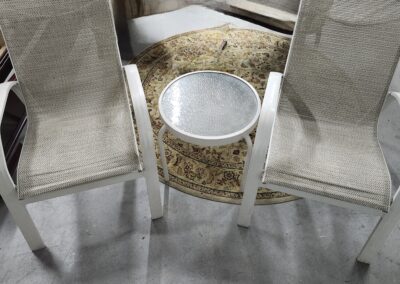 Two beige chairs with a round glass-topped table in between on a gray floor.