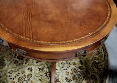 Antique wooden round side table with leather top on ornate rug.