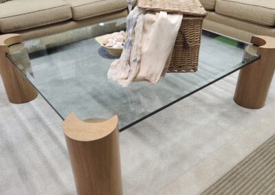 Modern glass coffee table with wooden cylindrical legs in a cozy living room.