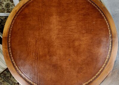 Top view of a round, brown leather ottoman with stitched detailing.