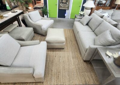 Modern living room set with light gray sofas, armchairs, and ottoman on a natural fiber rug.