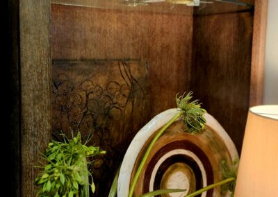Decorative wooden bow and arrow set displayed on a wooden shelf with plants and a lamp.