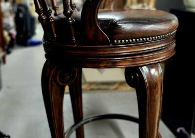 Elegant wooden bar stool with leather seat and ornate carvings.
