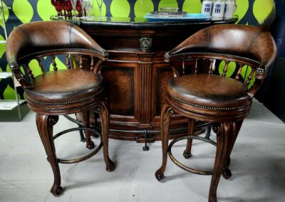 Two vintage wooden bar stools in front of a dark wood bar counter.