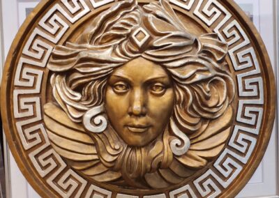Intricate golden Medusa head sculpture framed by a Greek key pattern.