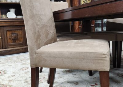 Beige upholstered dining chair with wooden legs next to a dark wood table.