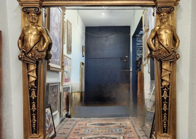 Ornate antique mirror with gold and black detailing in a hallway.