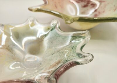 Two iridescent glass bowls with wavy edges on a light background.