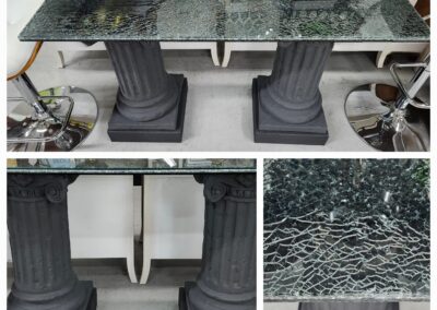 A glass table with ornate black pedestal bases and a cracked glass top.