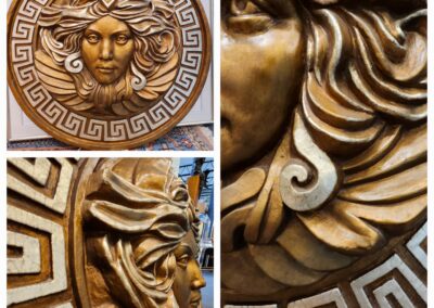 Intricately carved wooden Medusa face with Greek key border.