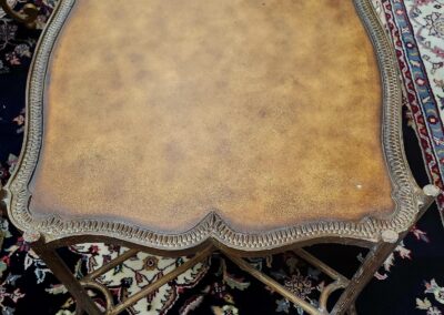 Antique wooden side table with intricate carvings and a worn leather top.