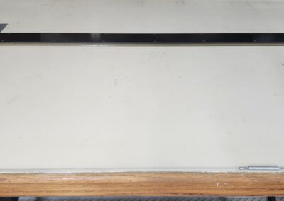 A blank whiteboard mounted on a wall with a wooden ledge below it.