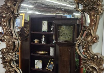 Ornate vintage mirror reflecting a room with shelves and framed pictures.