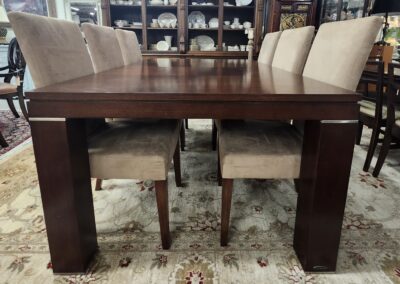 Wooden dining table with six beige upholstered chairs on a patterned rug.