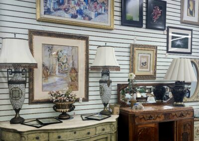 An antique furniture display with framed artwork and decorative lamps.