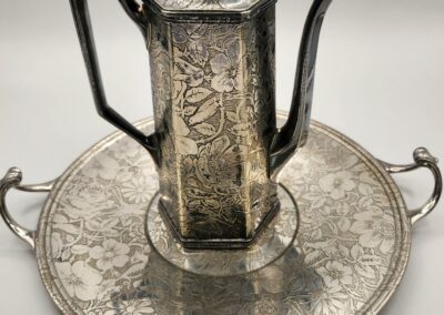 Intricately designed silver teapot with matching tray, featuring ornate floral engravings.
