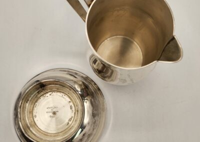 Top view of a silver pitcher and its lid on a white surface.
