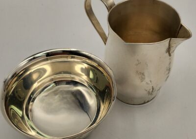 Polished silver bowl and pitcher on a plain surface.