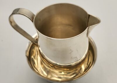 A brass pitcher with a handle and spout sitting on a matching brass saucer.