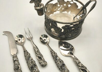 Intricately designed antique silverware set with ornate handles and a decorative cup holder.