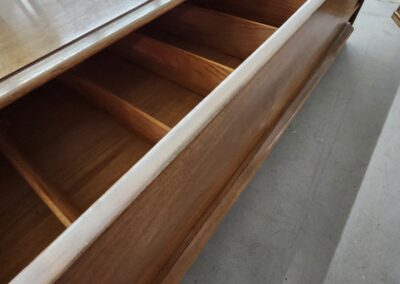 Open wooden drawer with multiple compartments inside a cabinet.