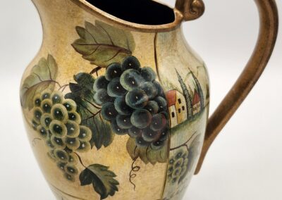 Decorative ceramic pitcher with grapevine and countryside motifs.