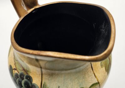 Hand-painted ceramic pitcher with a scenic design and a golden handle.