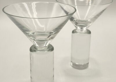 Two modern clear glass martini glasses with cylindrical stems.