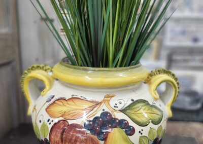 Colorful ceramic pot with fruit designs and green plants.