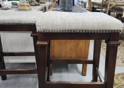 Wooden stool with beige cushion in a vintage furniture setting.