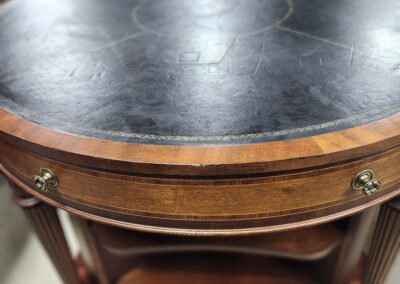 Round wooden table with a leather top and brass accents.