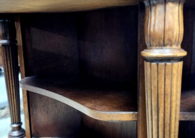 Antique wooden shelf with ornate column detail and curved edges.