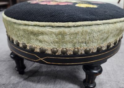 Close-up of an antique upholstered stool with decorative tacks and wooden legs.
