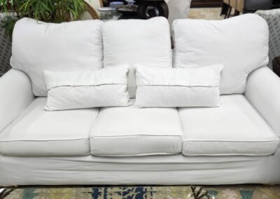 A white three-seater sofa with cushions on a blue and beige rug.