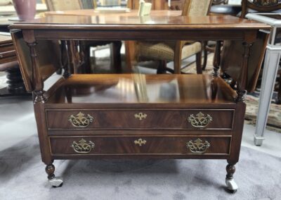 Antique wooden table with two drawers and brass handles on wheels.
