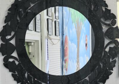 Black ornate round mirror with a leafy frame reflecting a colorful mural.