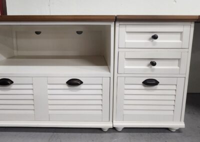 White wooden cabinet with louvered doors and drawers with black knobs.