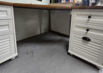 Empty space under a wooden desk with white drawers on a gray carpet.