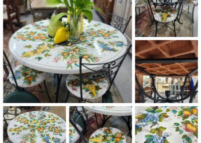 A round mosaic table with a floral and lemon design, supported by a black metal frame.
