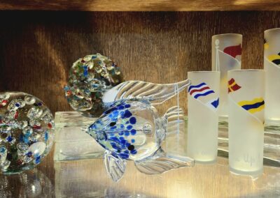 Glass fish sculpture with colorful accents on a wooden shelf.