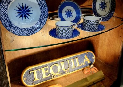 Vintage wooden shelf displaying blue-patterned cups and a 'TEQUILA' sign.