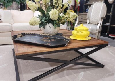 Modern wooden coffee table with a metal X-frame base and decorative items on top.